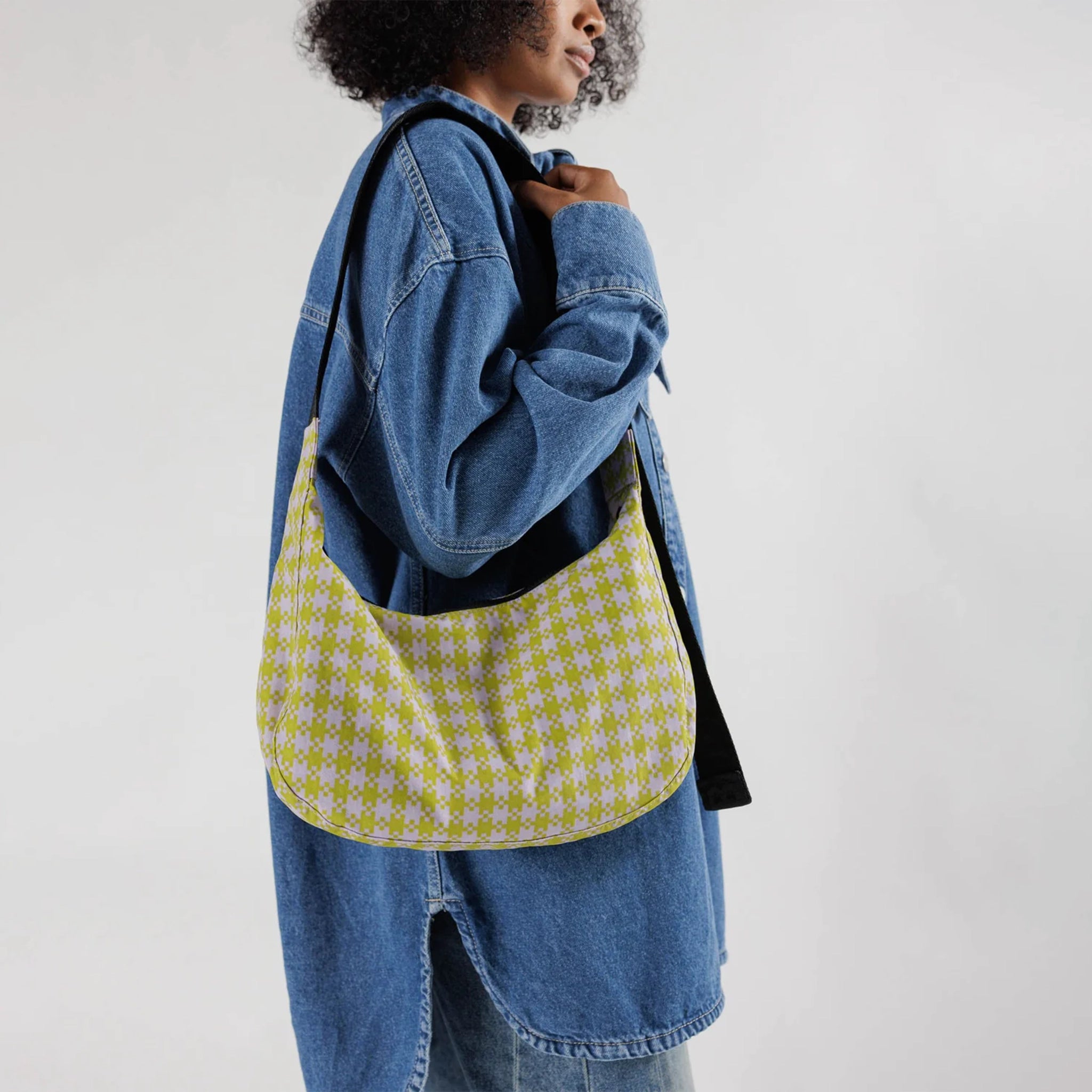 A light pink and lime green gingham nylon crescent shaped bag with an adjustable black strap that reads, "BAGGU" in black and a single zipper.