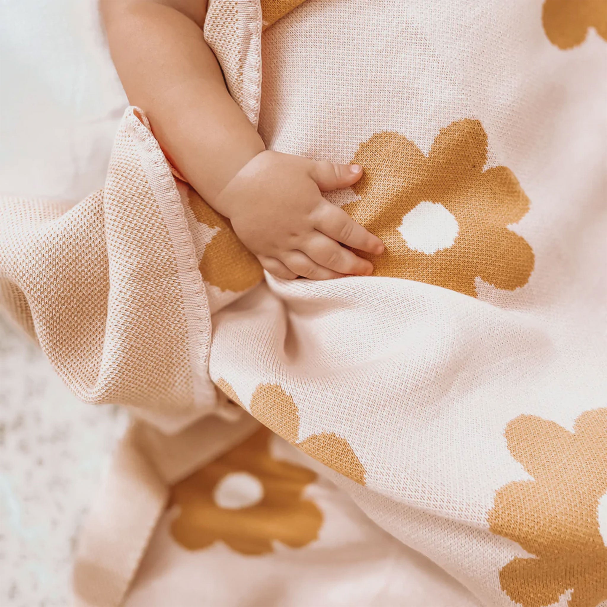 A light blush cotton blanket with a repeating mustard yellow daisy print.
