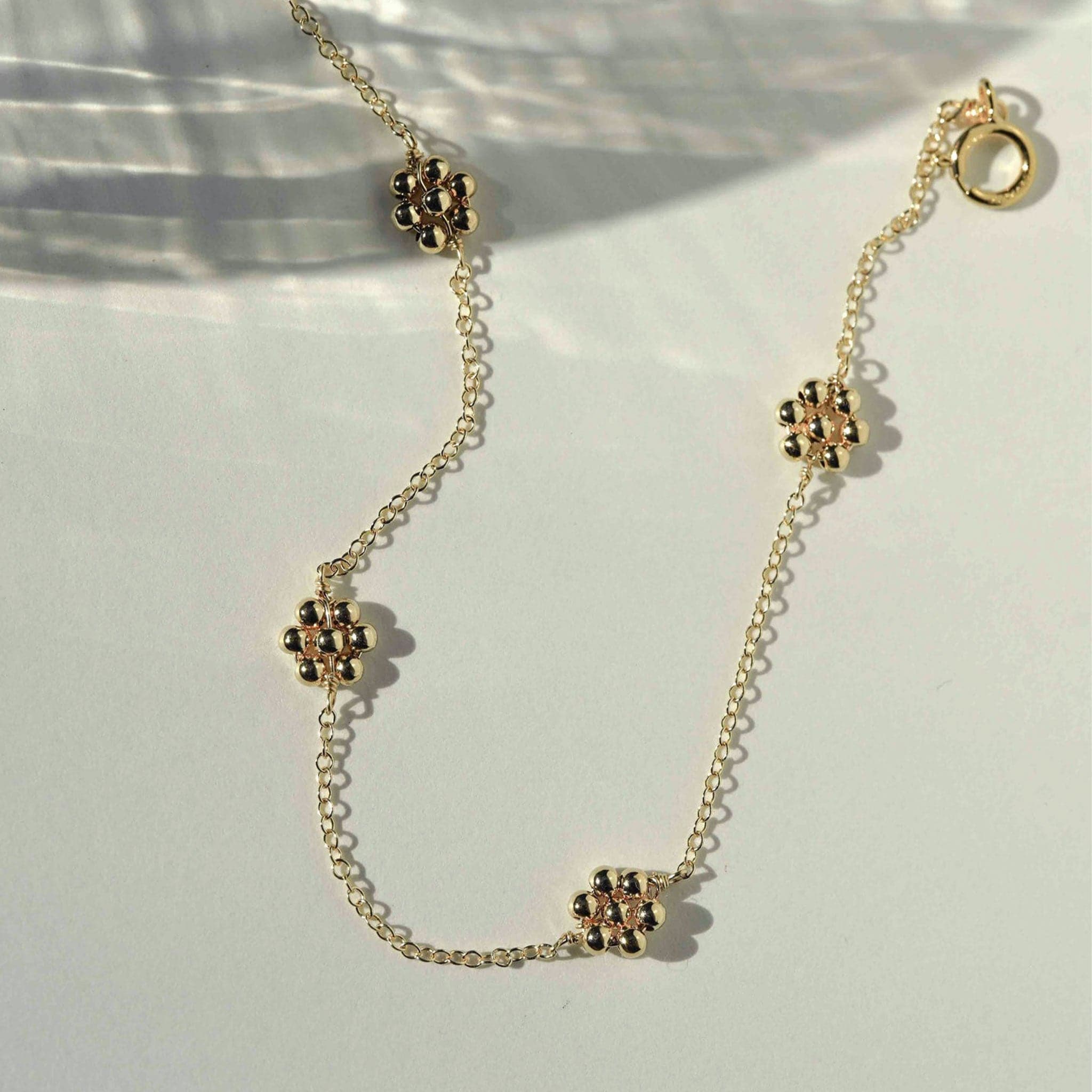 A dainty gold chain bracelet with four gold beaded daisies evenly placed on the chain.