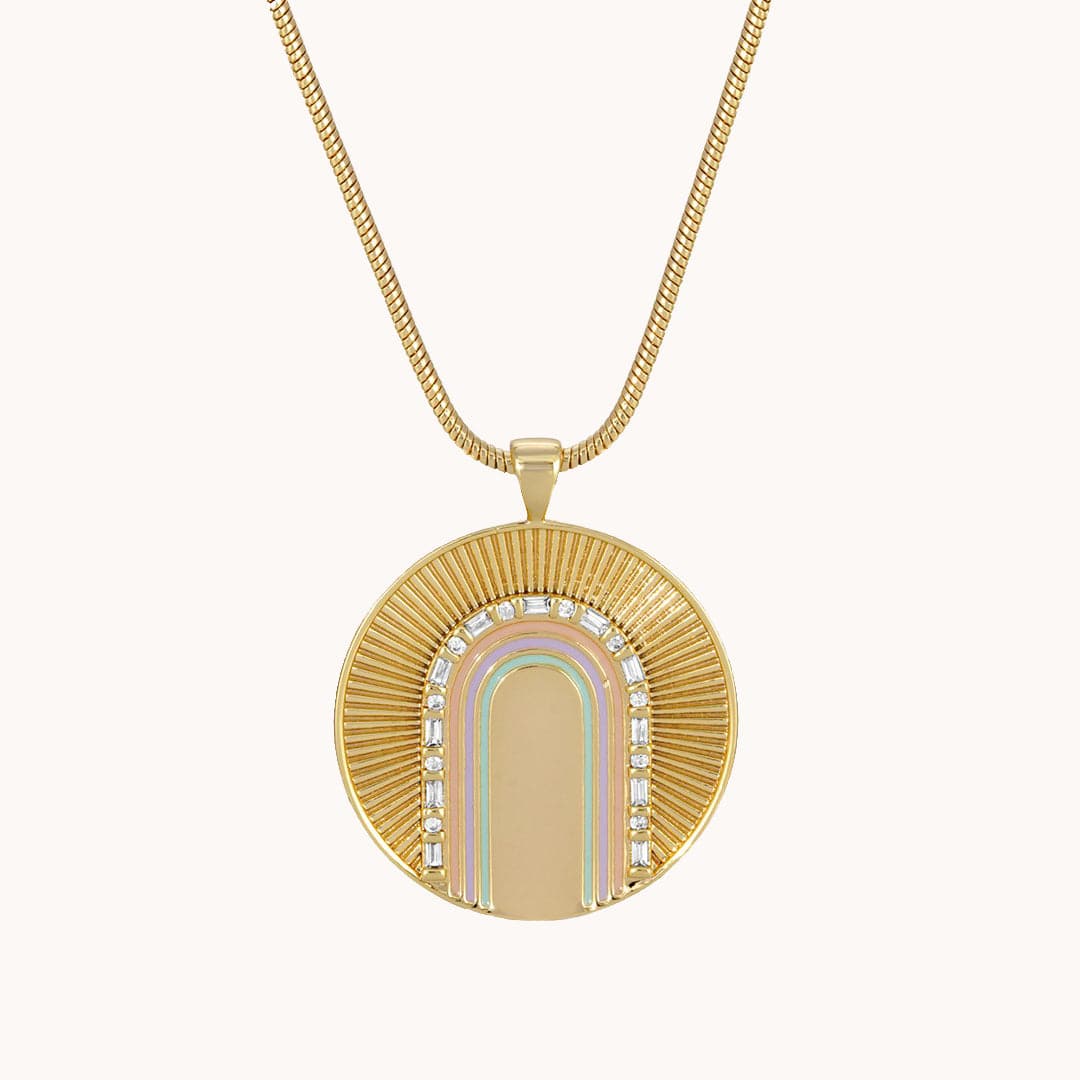A gold pendant necklace with sun rays beaming from a gem stones arch, and underneath orange, purple, and green rainbow arches.