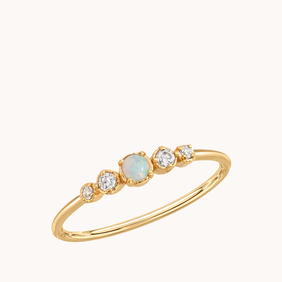 In front of a white background is a gold ring with a green opal in the middle. On each side of the opal is two clear stones. 
