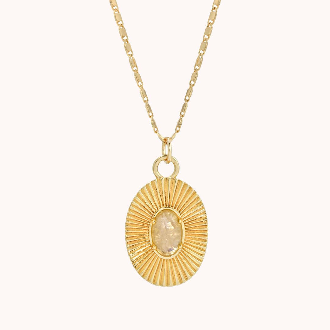 Gold oval pendant with set clear crystal gemstone in center and gold indentations like sun rays in the gold pendant.