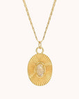Gold oval pendant with set clear crystal gemstone in center and gold indentations like sun rays in the gold pendant.