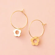 On a peachy background is a dainty gold hoop earring with a smaller daisy charm dangling from the bottom edge.