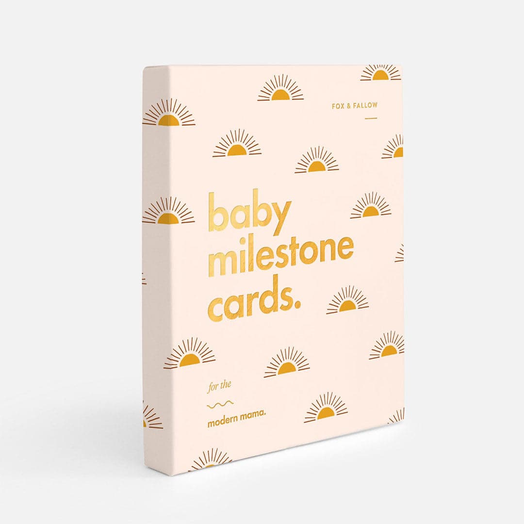 Ivory book with gold sun illustration and gold foil text "Baby Milestone Cards - For the modern mama"