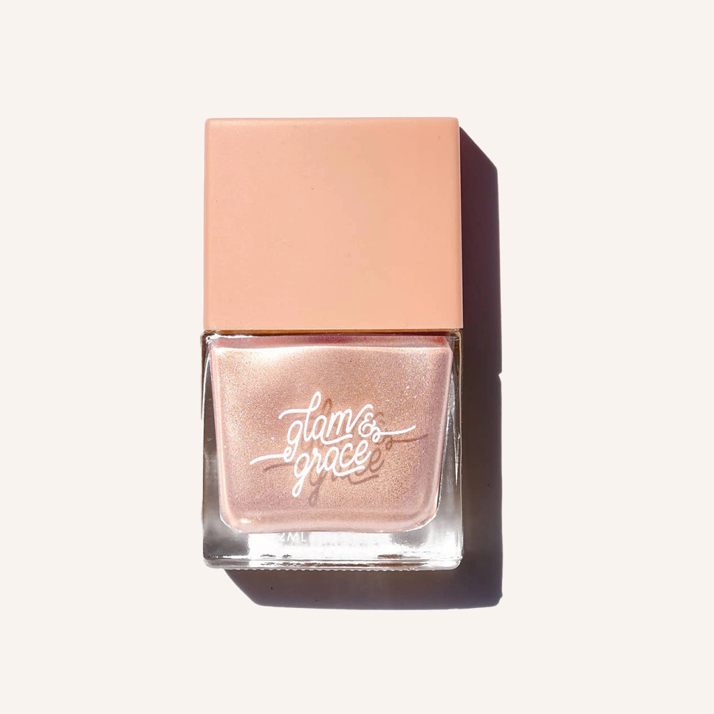 A shimmering cream nail polish with rose gold glitters in a glass bottle with a square peach lid.