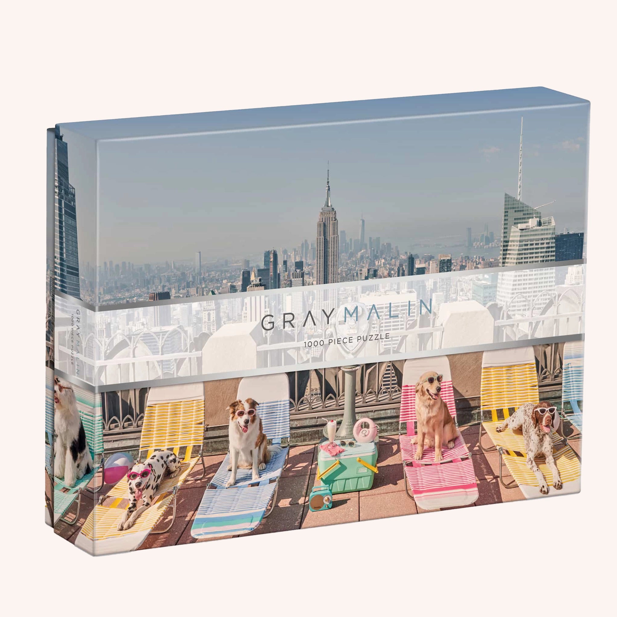 A puzzle in a box with a photograph of New York City with different breeds of dogs wearing sunglasses and sitting on a rooftop on sun chairs.