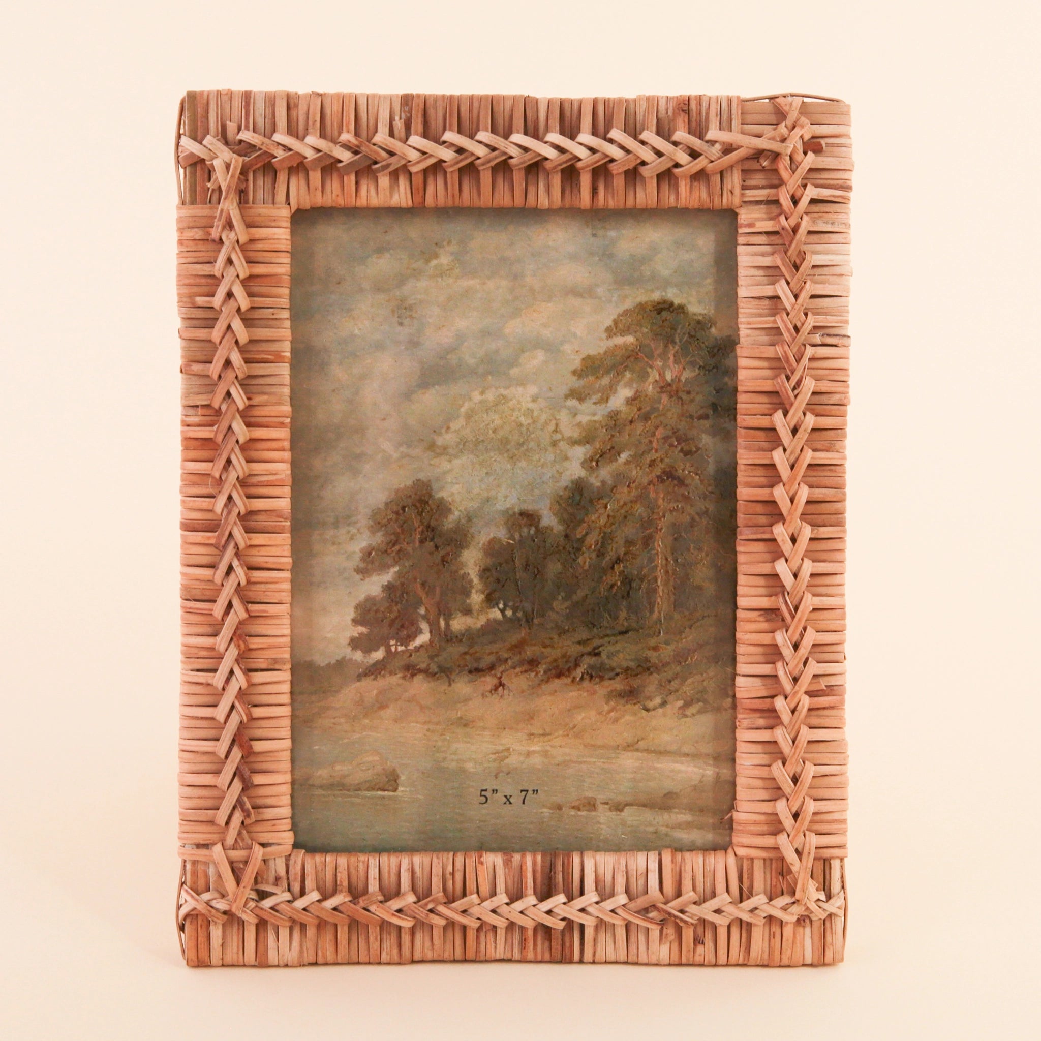 Photographed on a cream background is a 5&quot; x 7&quot; hand woven rattan frame a natural brown shade detailed with intricate stitching int he center.