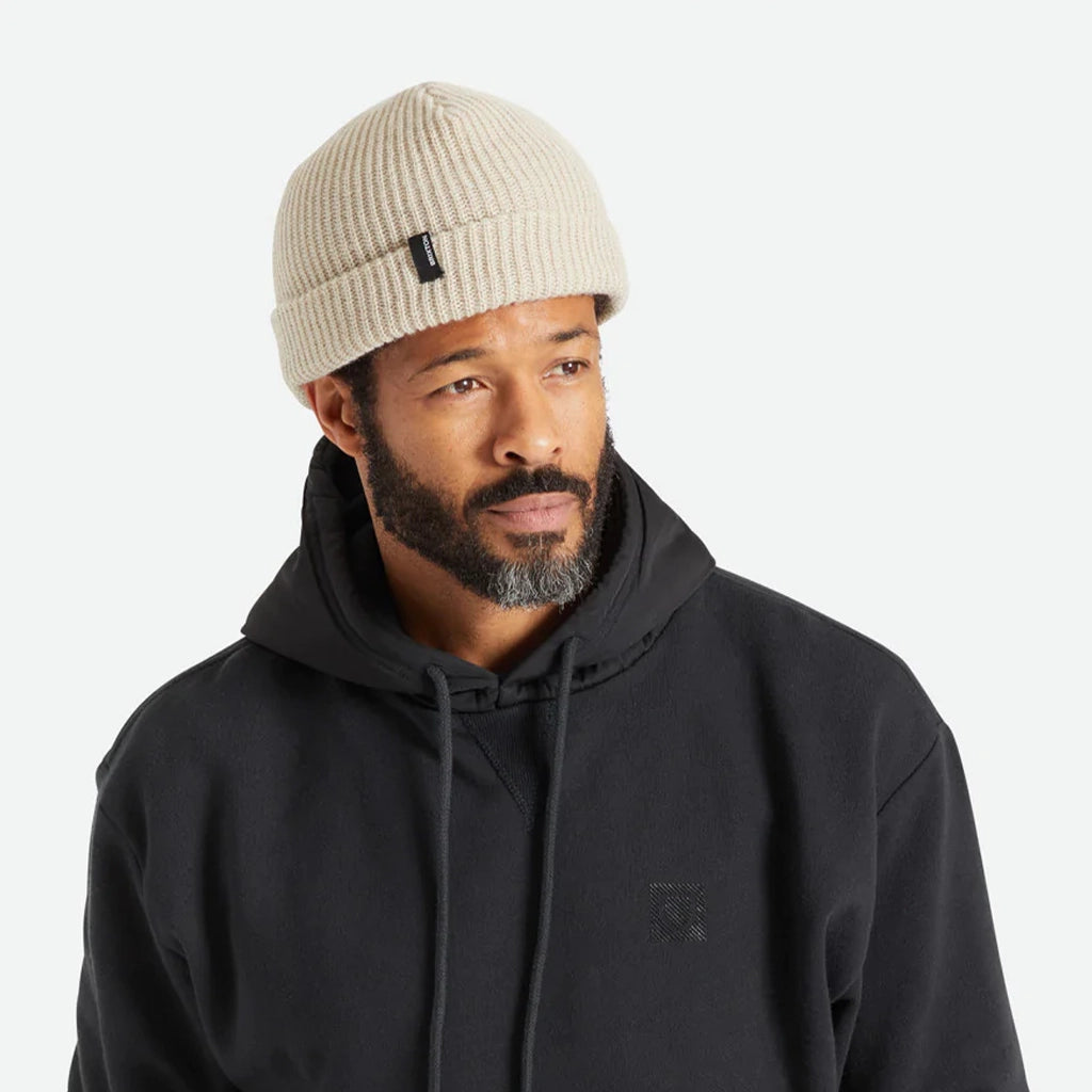 A knit ribbed beanie in a beige color with a folded brim and a black label on the front right left corner.