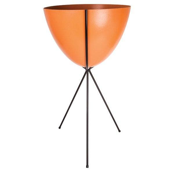 In front of a white background is an orange colored bullet planter. The planter has a wide top and narrows at the bottom. The planter is held up by a black metal stand. The stand has three black metal legs.