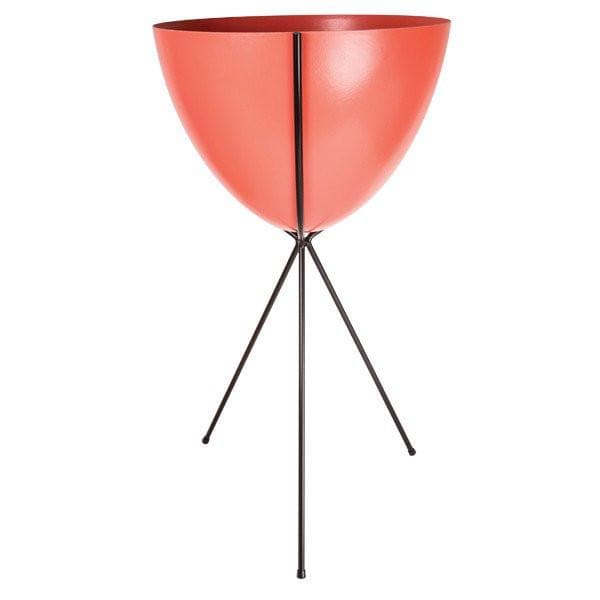 In front of a white background is a red colored bullet planter. The planter has a wide top and narrows at the bottom. The planter is held up by a black metal stand. The stand has three black metal legs.