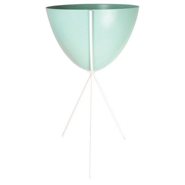 In front of a white background is a turquoise colored bullet planter. The planter has a wide top and narrows at the bottom. The planter is held up by a white metal stand. The stand has three white metal legs.
