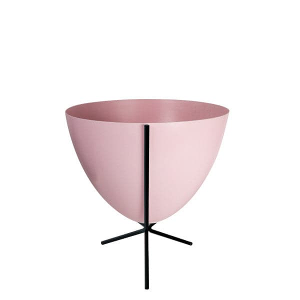 In front of white background is a soft pink planter in a short black metal stand. The bullet planter is wide at the top and narrow at the bottom. The metal stand has three legs. 
