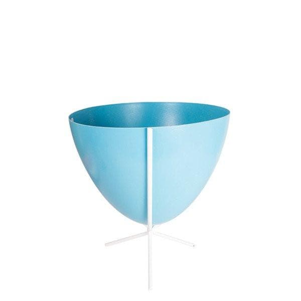 In front of white background is a bright blue bullet planter in a short white metal stand. The bullet planter is wide at the top and narrow at the bottom. The metal stand has three legs. 