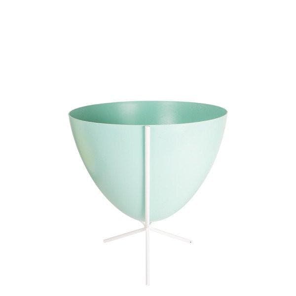 In front of white background is a turquoise bullet planter in a short white metal stand. The bullet planter is wide at the top and narrow at the bottom. The metal stand has three legs. 