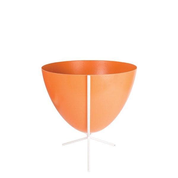 In front of white background is an orange planter in a short white metal stand. The bullet planter is wide at the top and narrow at the bottom. The metal stand has three legs.
