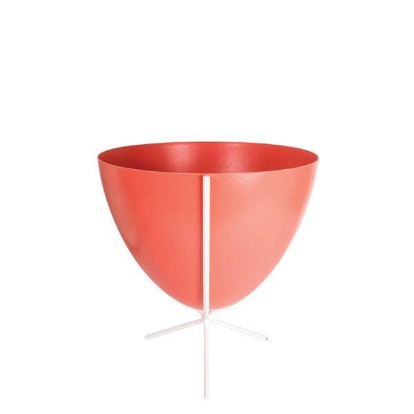 In front of white background is a red planter in a short white metal stand. The bullet planter is wide at the top and narrow at the bottom. The metal stand has three legs. 