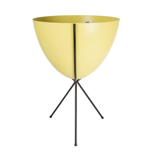 In front of white background is a yellow planter in a black metal stand. The bullet planter is wide at the top and narrow at the bottom. The metal stand has three legs. 