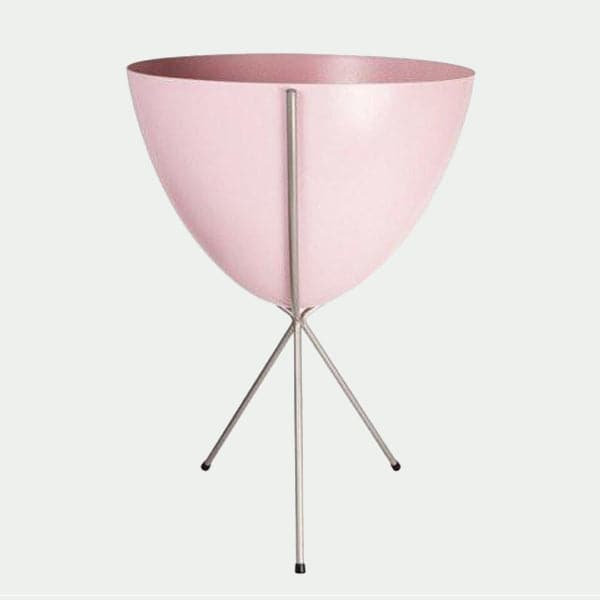 In front of white background is a soft pink planter in a silver metal stand. The bullet planter is wide at the top and narrow at the bottom. The metal stand has three legs. 