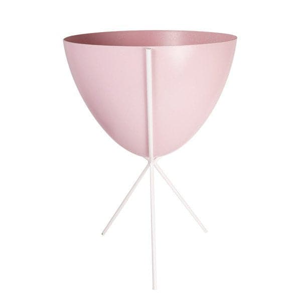 In front of white background is a soft pink planter in a white metal stand. The bullet planter is wide at the top and narrow at the bottom. The metal stand has three legs.
