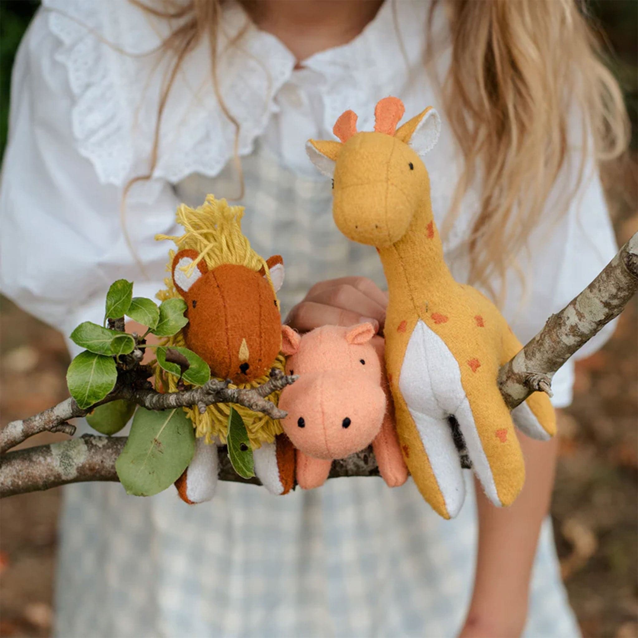 A stuffed animal set inspired by the Savannah. It includes a pink hippo, a red lion with a yellow mane, and a mustard yellow giraffe with orange spots and an orange tail.