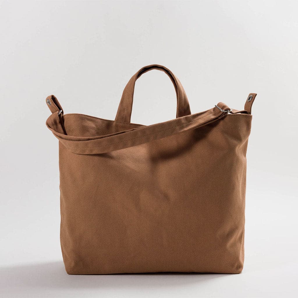 This canvas tote is coffee brown and square shaped. The bag is complete with both two smaller handles and one large shoulder strap in the same color.