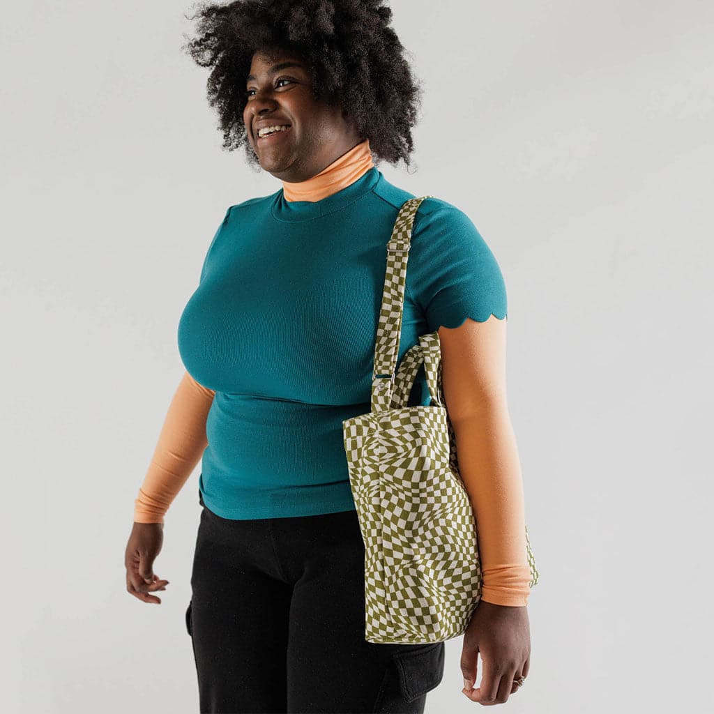 Model standing with the checkered bag hanging from her shoulder. There are wearing a teal t-shirt layered over an orange long sleeve. 