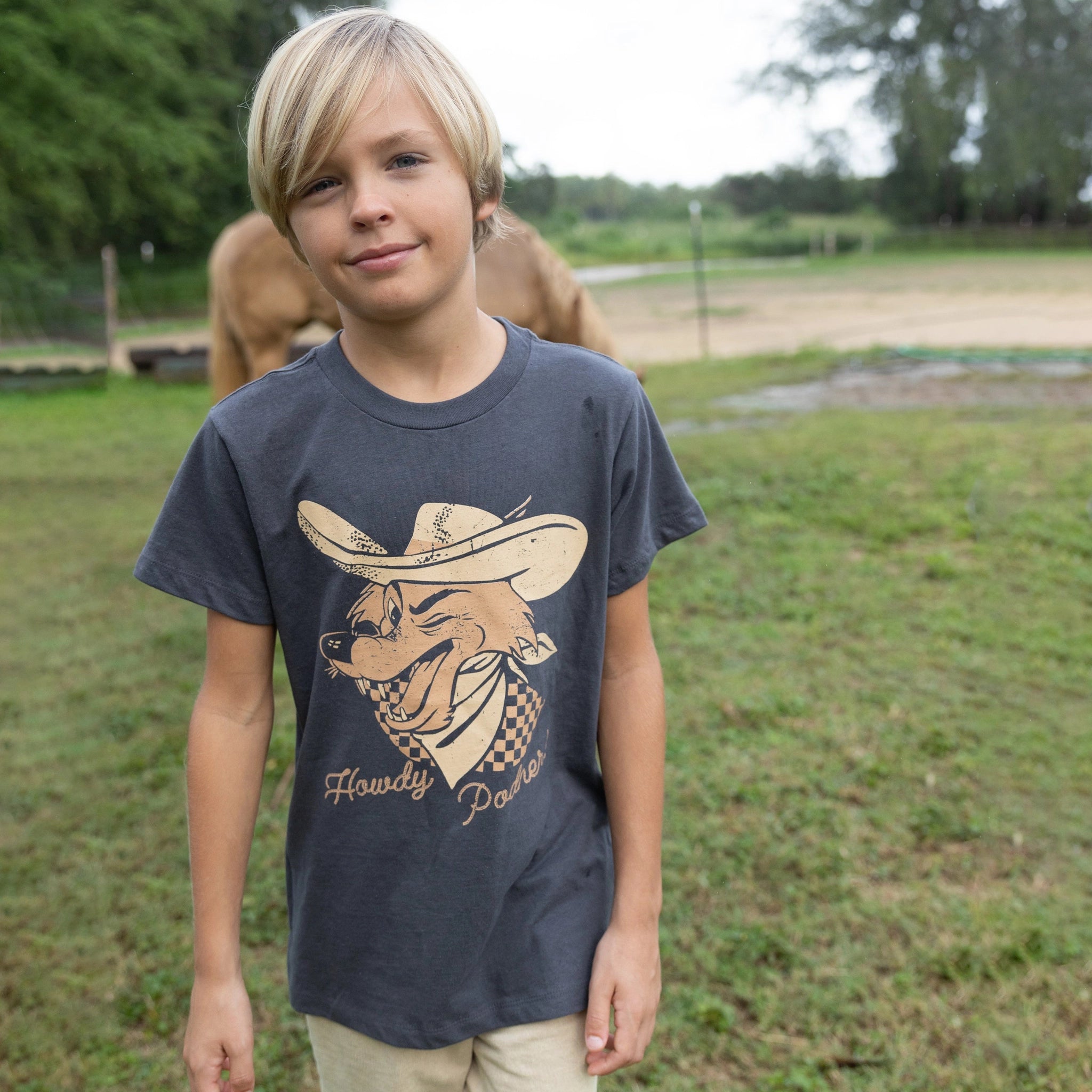 A model wearing a faded black t-shirt with a coyote graphic on the front wearing a cowboy hat and says, &quot;Howdy Cowboy&quot; in cursive text underneath the graphic. 