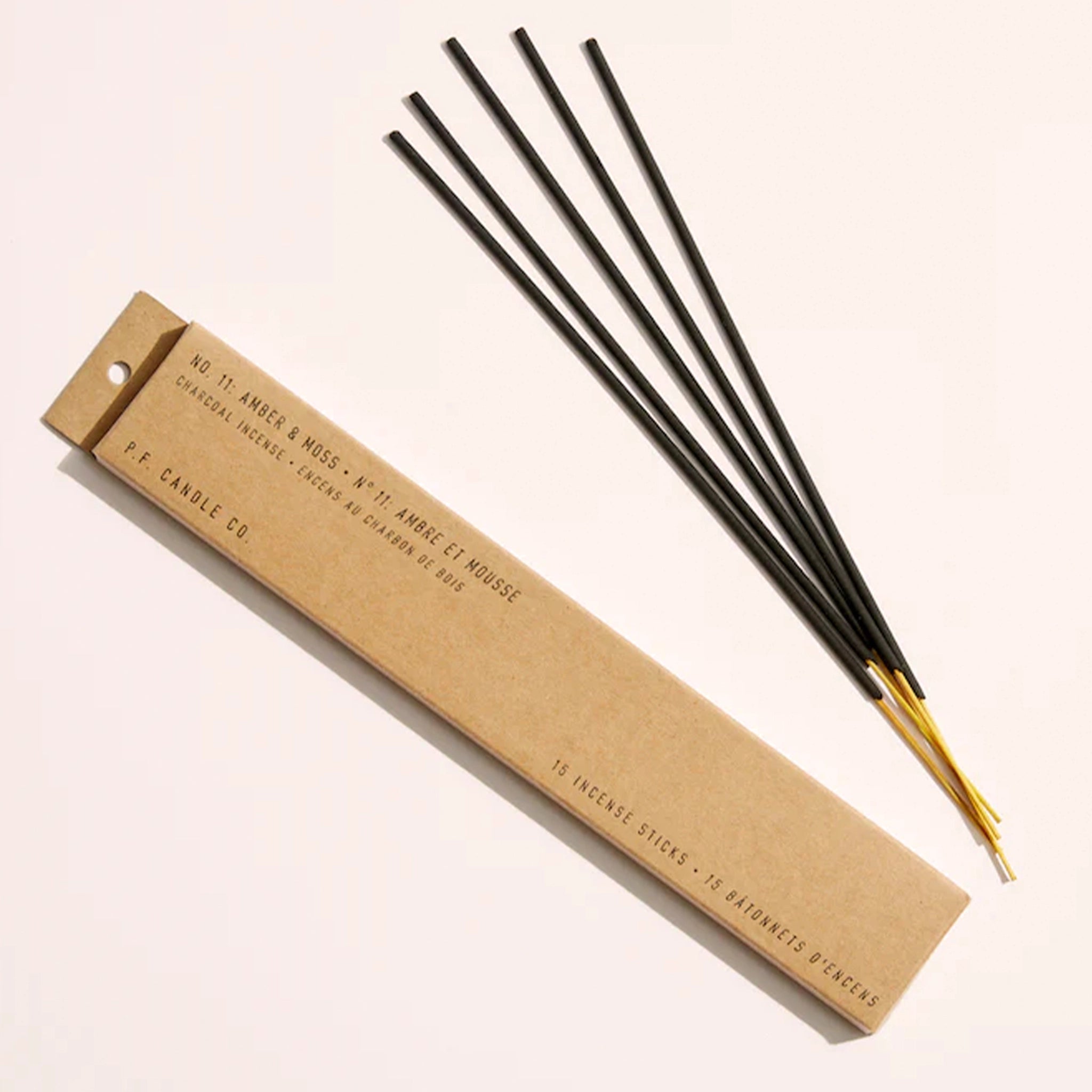 A cardboard package with 5 incense sticks with black ties and exposed natural wood ends along with black text on the box that reads, "Amber & Moss Charcoal Incense".