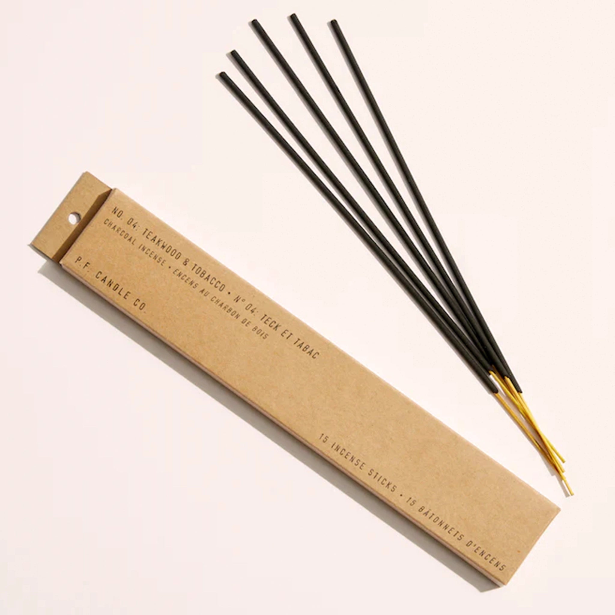 A cardboard package with 5 incense sticks with black ties and exposed natural wood ends along with black text on the box that reads, "Teakwood & Tobacco Incense".