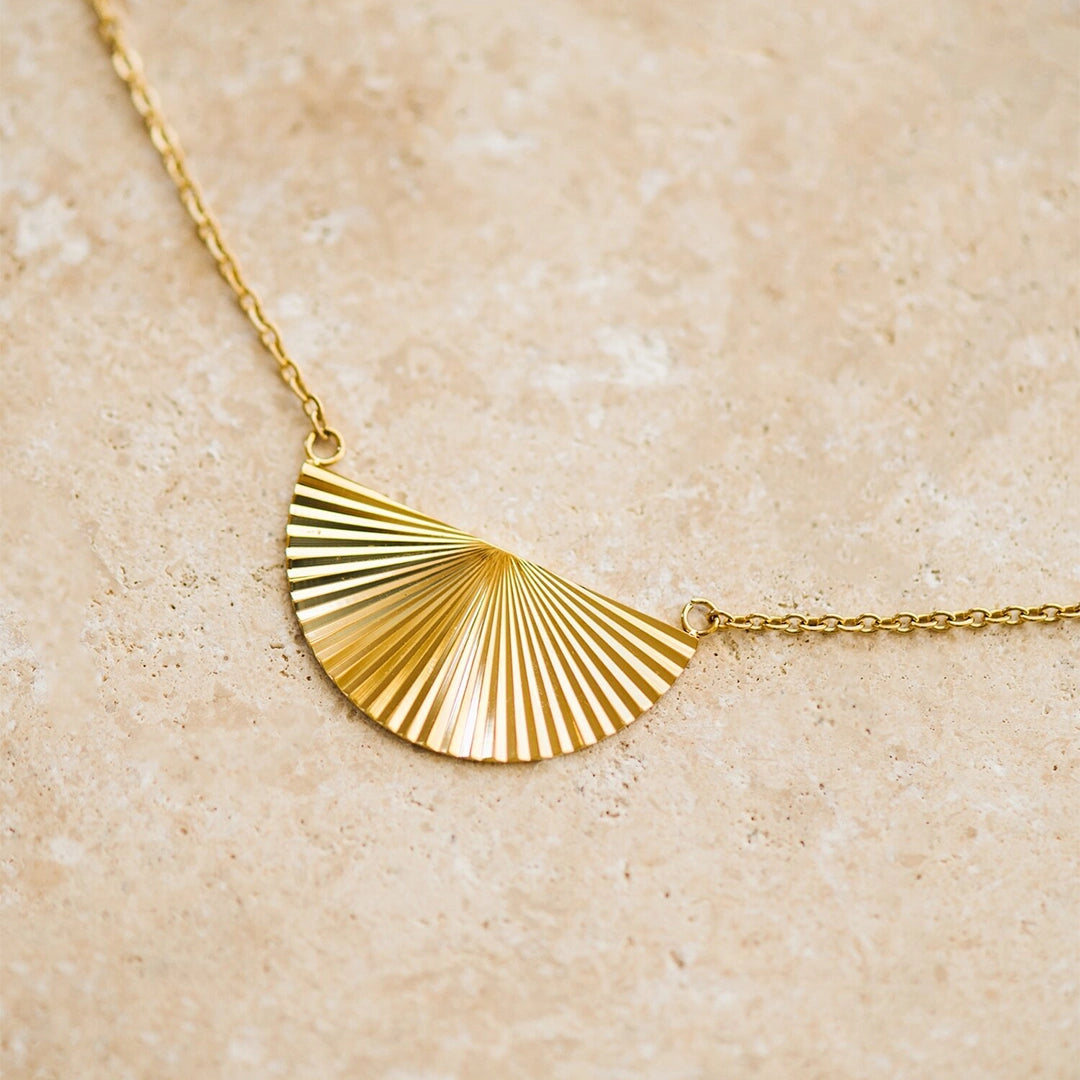 A thin gold necklace with a half sunburst pendant in the center.