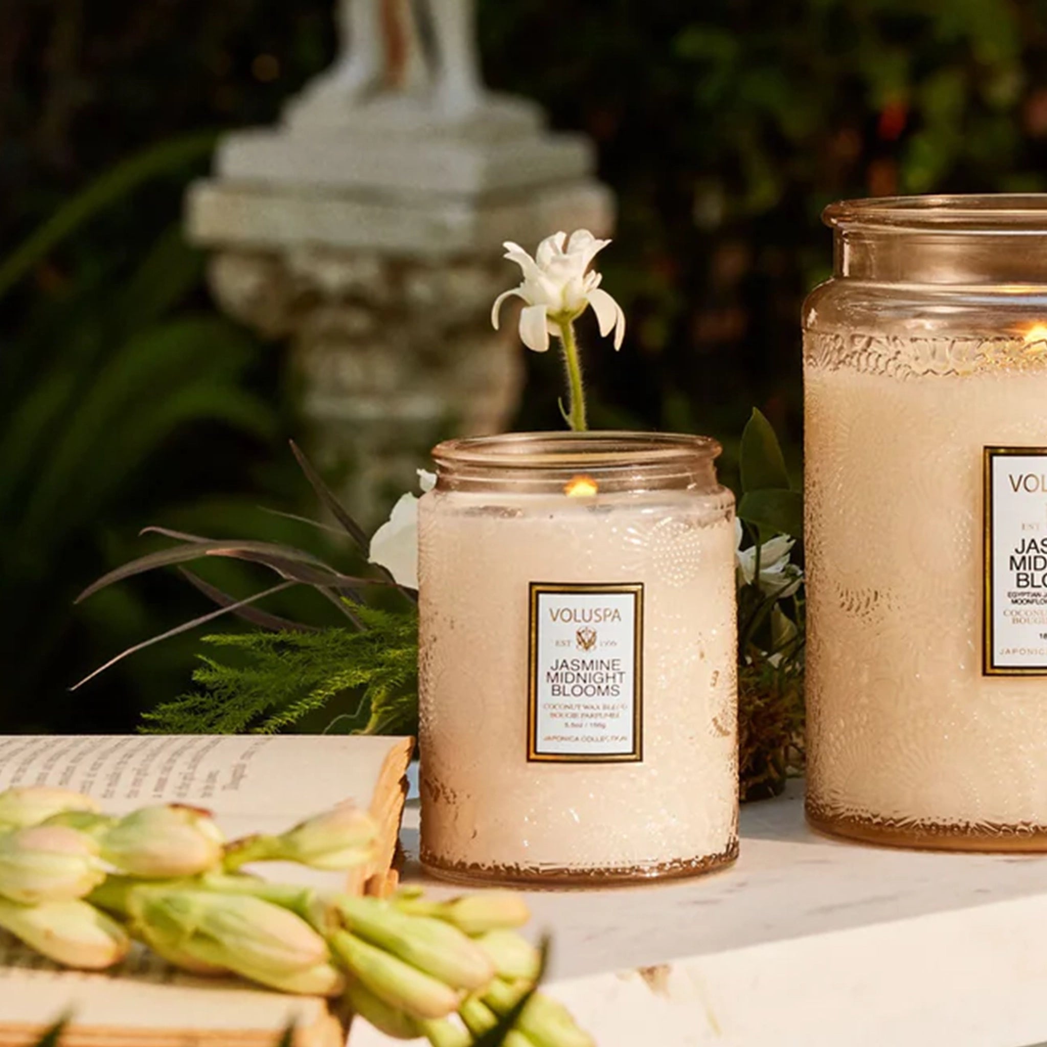 An apricot colored decorative glass jar candle with an etched floral pattern in the glass and a white rectangular label in the center that reads, "Jasmine Midnight Blooms".
