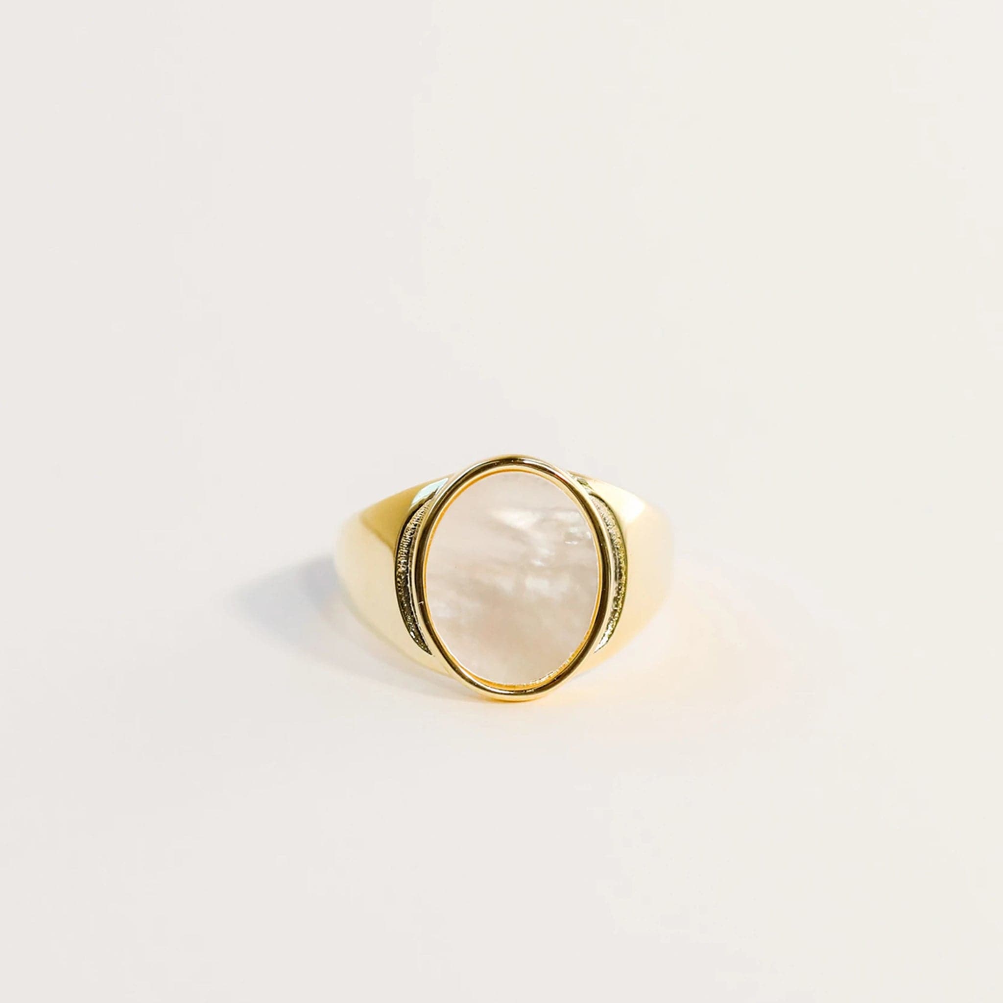 A statement gold signet ring with an oval mother of pearl stone set in the center.