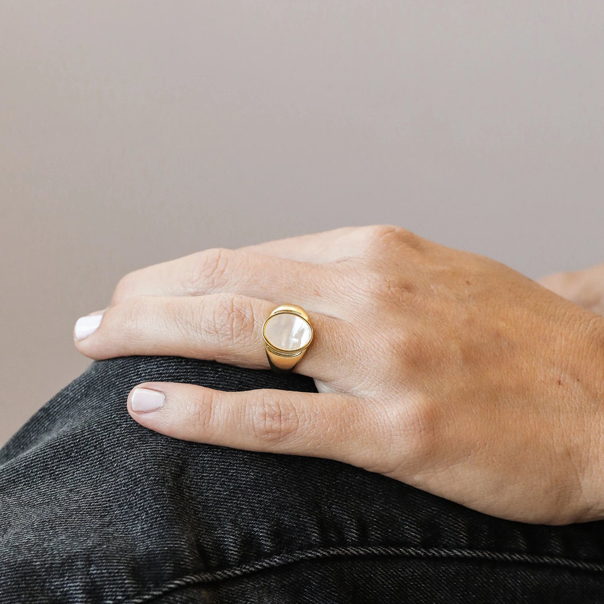 A statement gold signet ring with an oval mother of pearl stone set in the center. Model is wearing it alone.