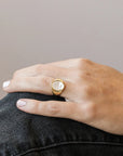 A statement gold signet ring with an oval mother of pearl stone set in the center. Model is wearing it alone.