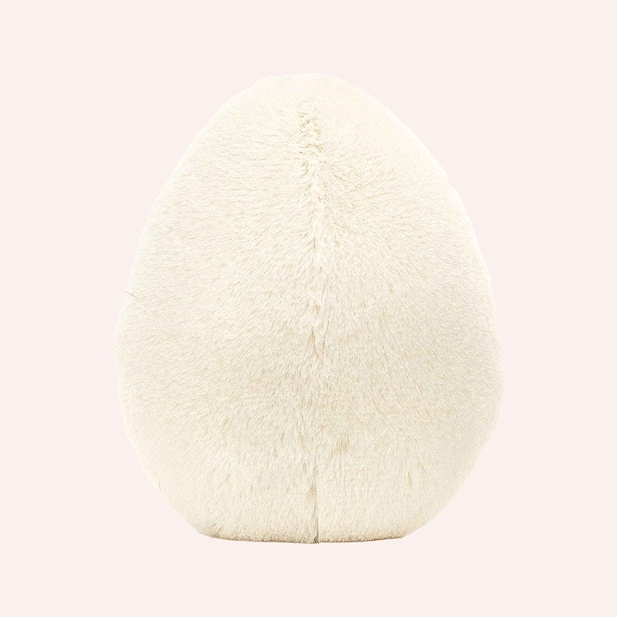 Back view of A soft stuffed animal in the shape of an egg with yellow yoke face and blushing smiley face, and brown floppy legs.