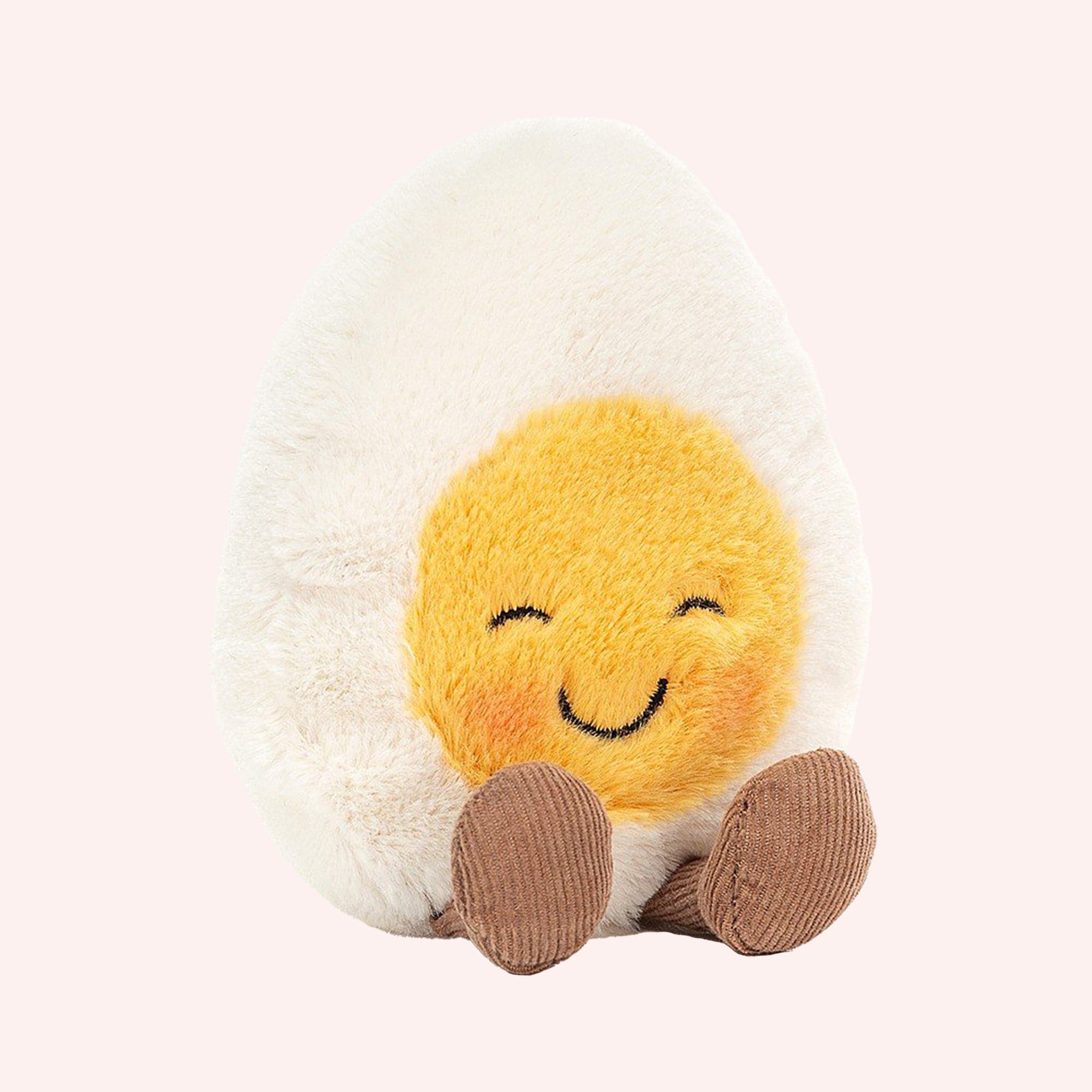 A soft stuffed animal in the shape of an egg with yellow yoke face and blushing smiley face, and brown floppy legs.
