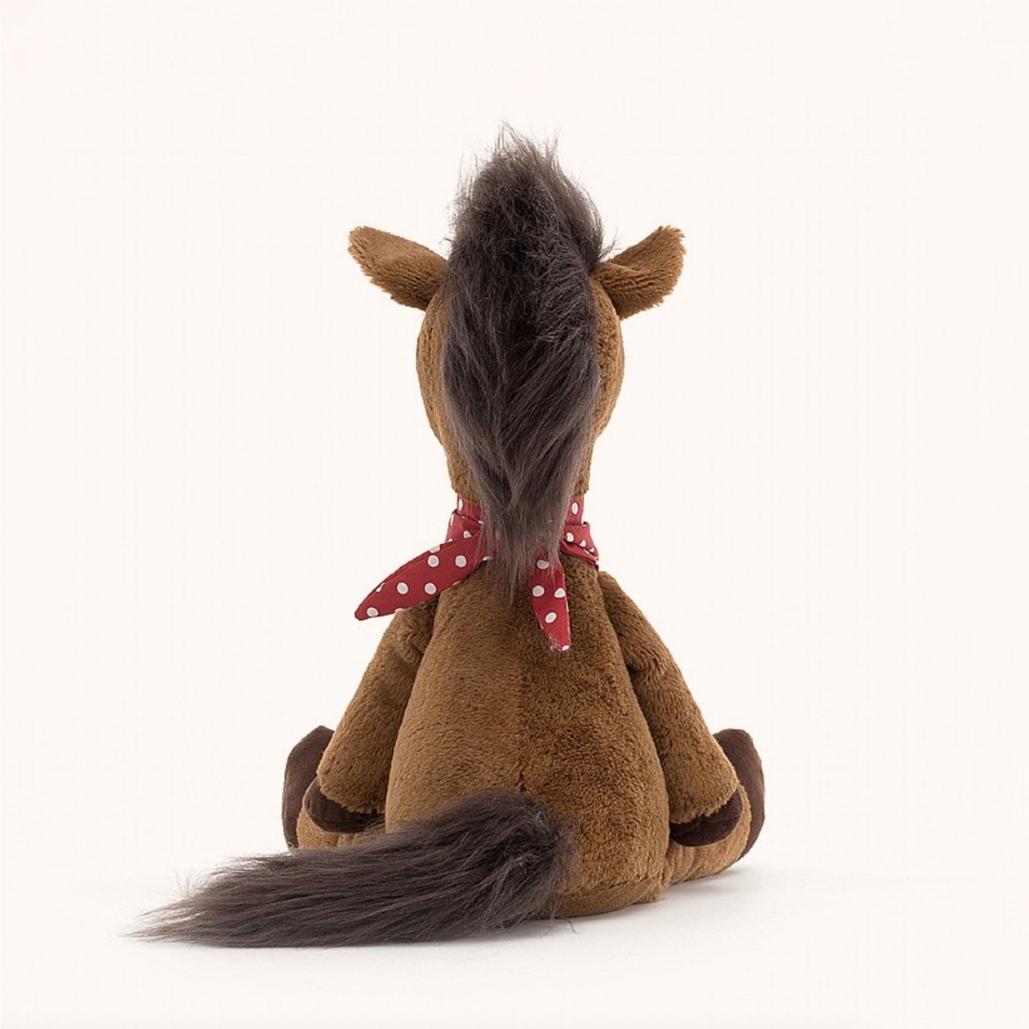 Soft stuffed animal in the shape of a brown horse with fluffy dark brown mane and tail, and wearing a red and white spotted bandana around its neck.