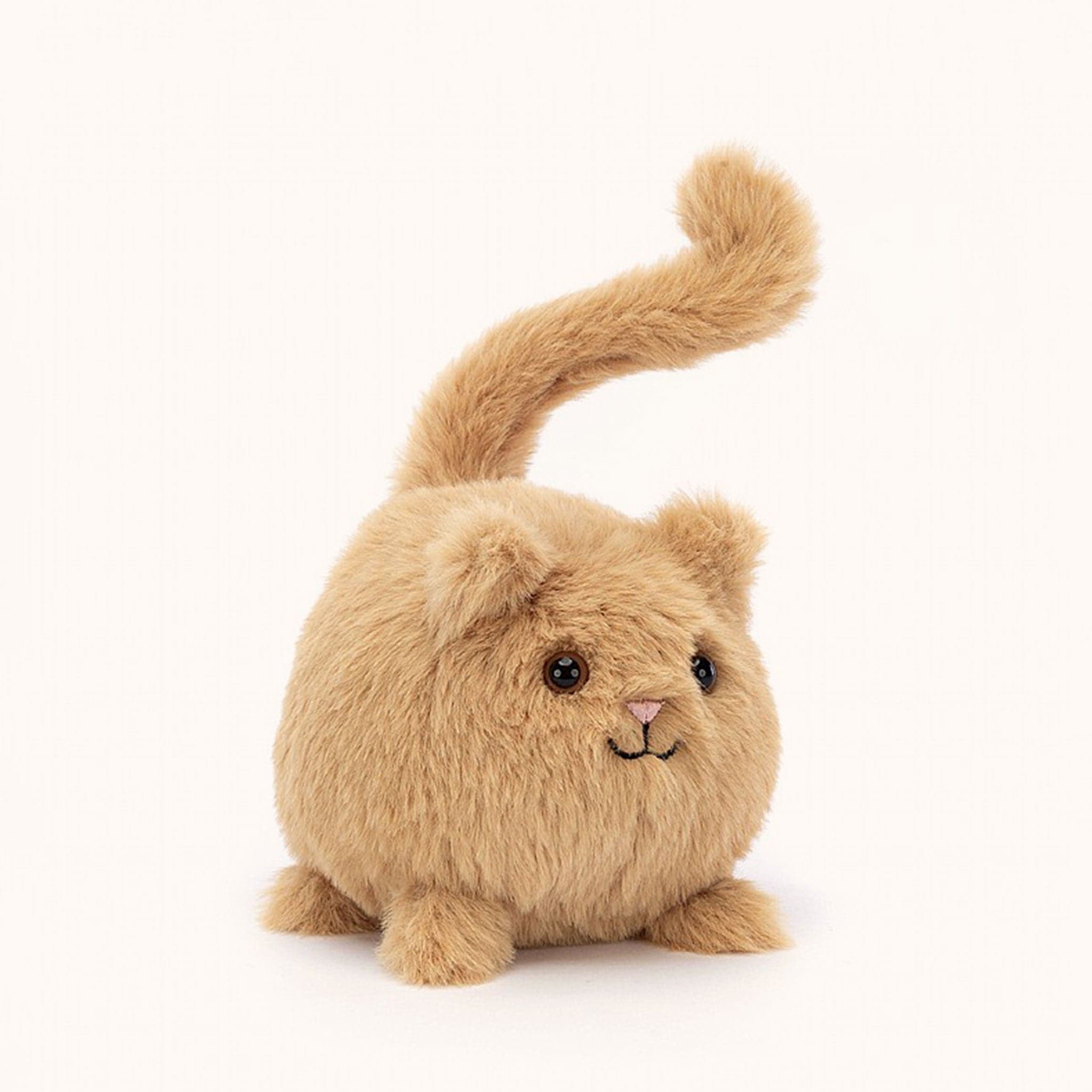 Soft stuffed animal in the shape of a round caramel colored cat with a question mark shaped tail.