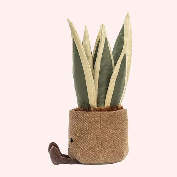 side view of a soft suede stuffed animal in the shape of a potted snake plant, with spikey dark and light green leaves, and brown textured pot with smiley face and dark brown floppy legs.