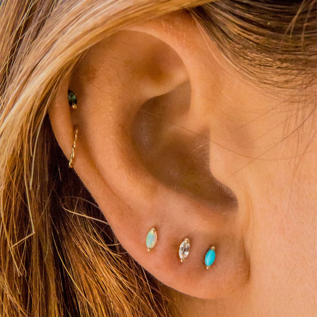 On a models ear is oval shaped stud earrings with an opal in the center. 