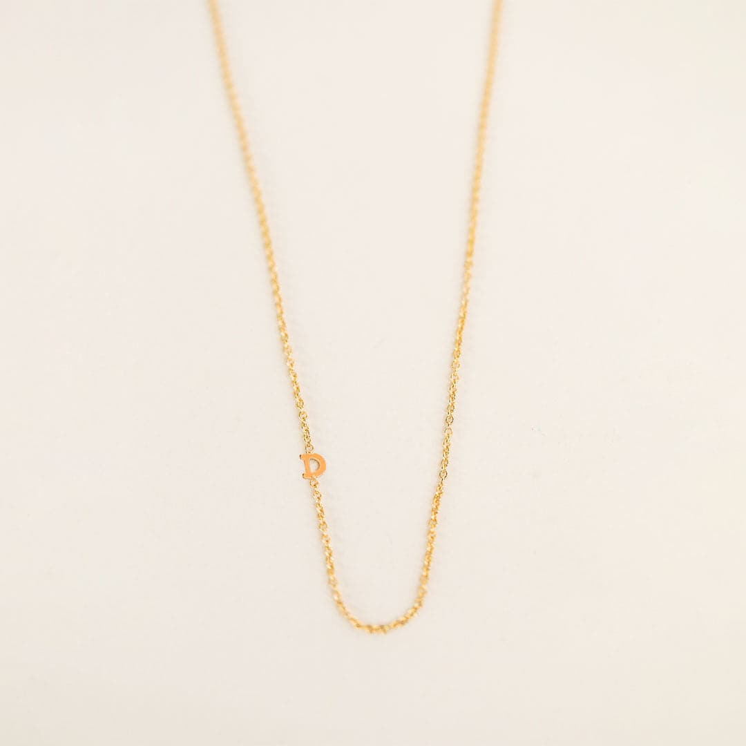 A dainty gold chain necklace with an "D" on the chain.
