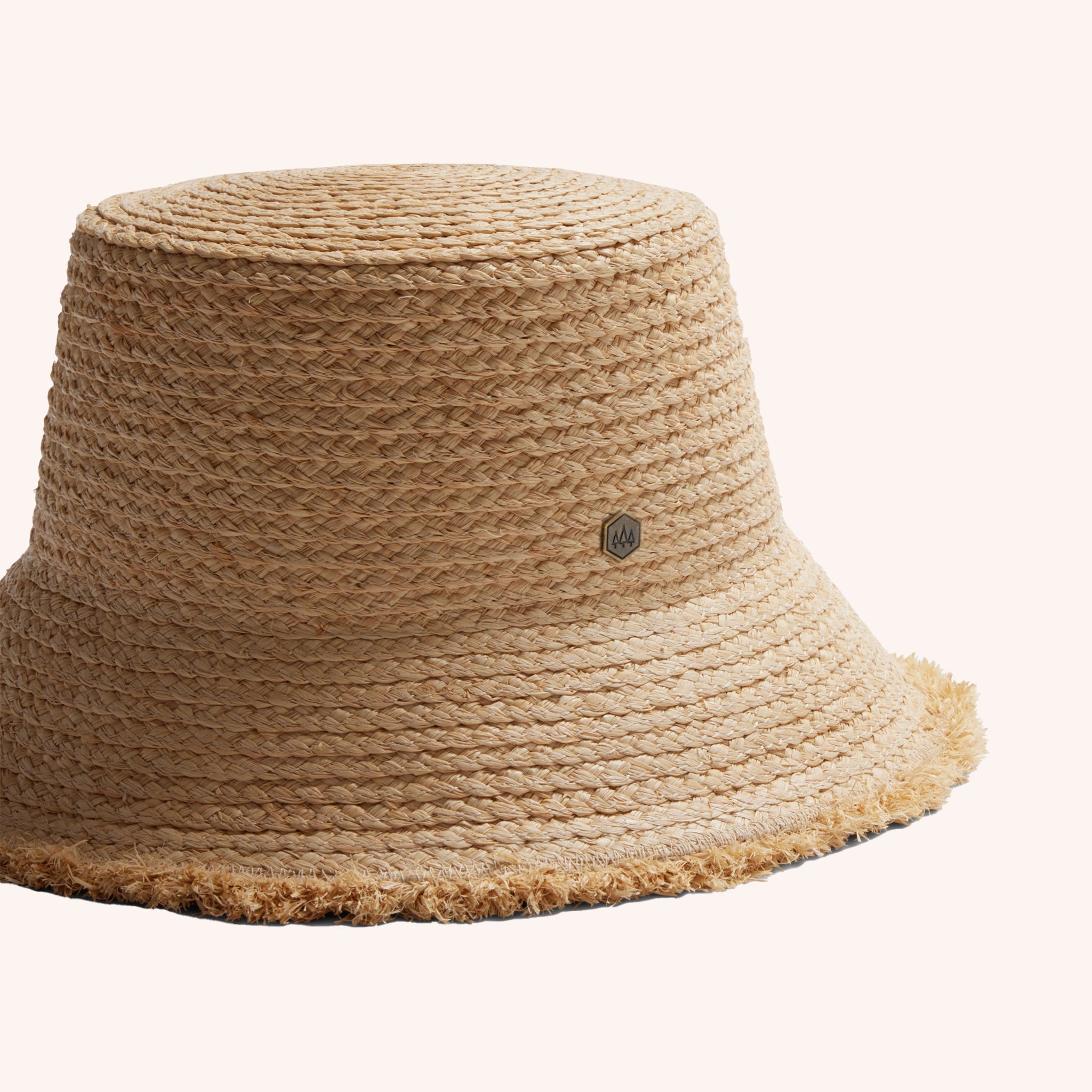 A woven bucket hat in a light straw color with a frayed edge detail along the edge of the brim and a tiny hemlock hat metal emblem in the center.