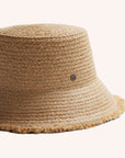 A woven bucket hat in a light straw color with a frayed edge detail along the edge of the brim and a tiny hemlock hat metal emblem in the center.