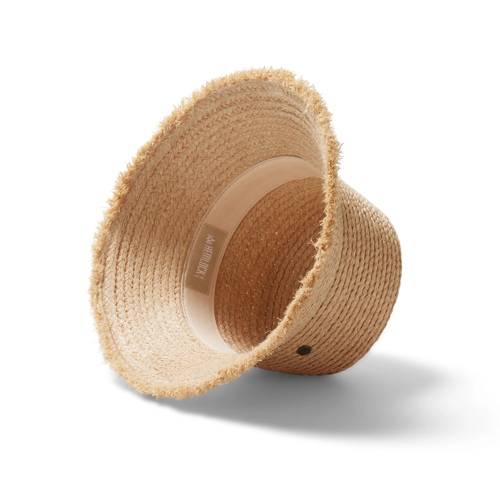A woven bucket hat in a light straw color with a frayed edge detail along the edge of the brim and a tiny hemlock hat metal emblem in the center.