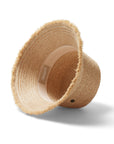 A woven bucket hat in a light straw color with a frayed edge detail along the edge of the brim and a tiny hemlock hat metal emblem in the center.