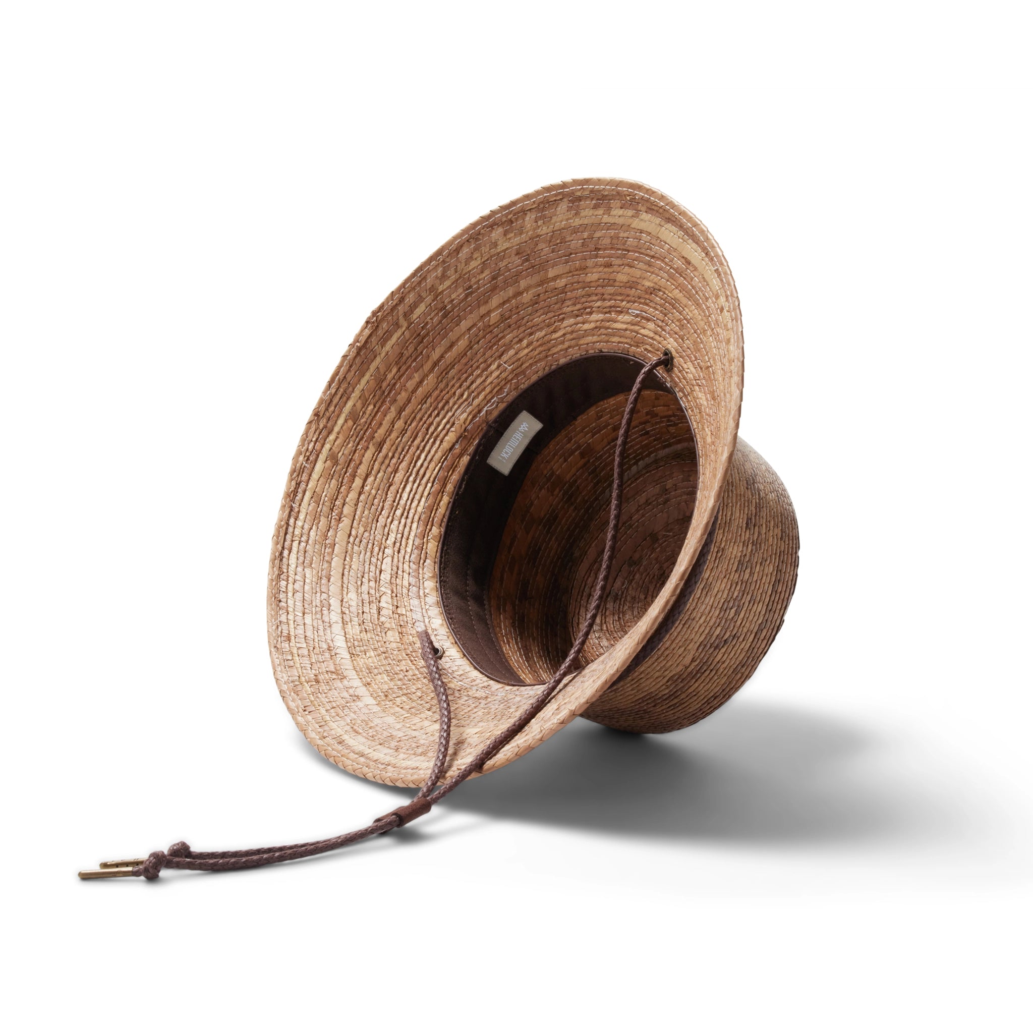 A woven bucket hat with a flat top, a slightly angled brim made of a darker brown straw and also features a brown drawstring.