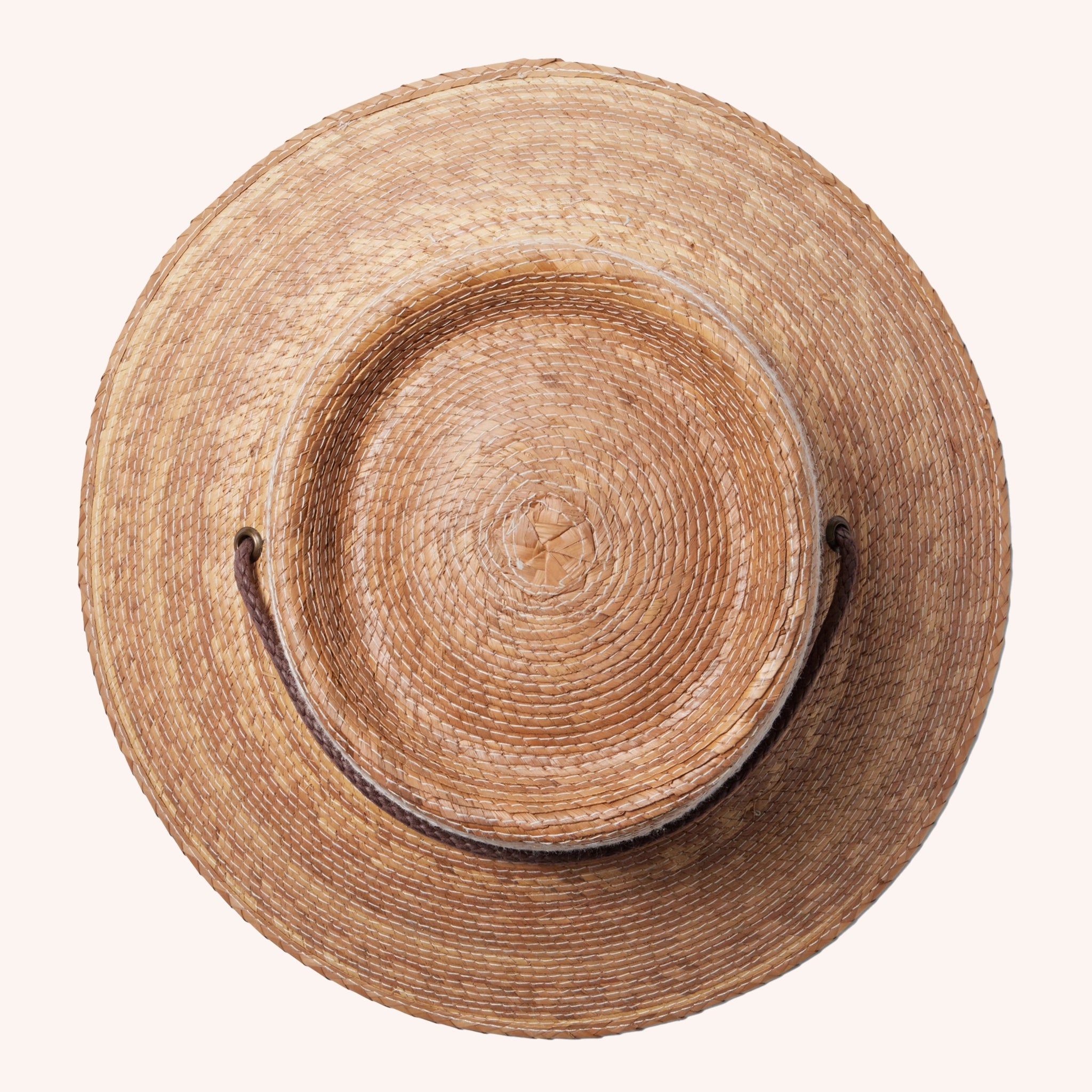 A woven bucket hat with a flat top, a slightly angled brim made of a darker brown straw and also features a brown drawstring.