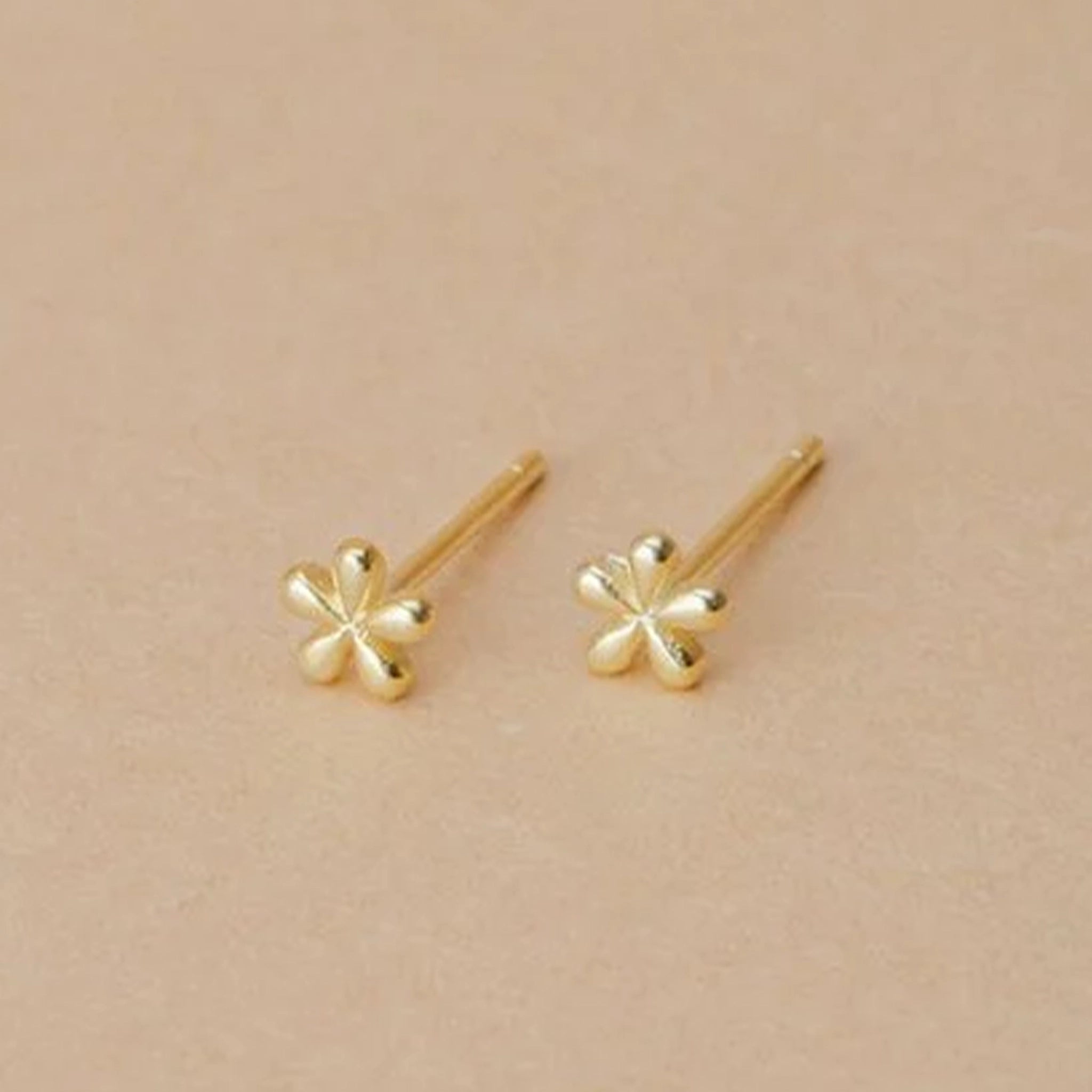 A pair of tiny gold daisy shaped stud earrings with a straight gold post.