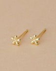 A pair of tiny gold daisy shaped stud earrings with a straight gold post.